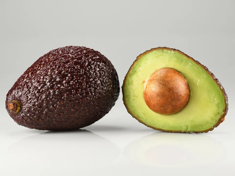Aguacate Hass entero y otro partido por la mitad, con la semilla a la vista, sobre fondo claro